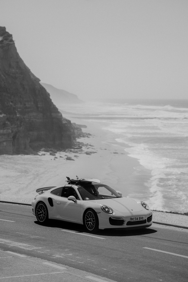 Black and white photograph of a sports car carrying surfboards beside the Atlantic